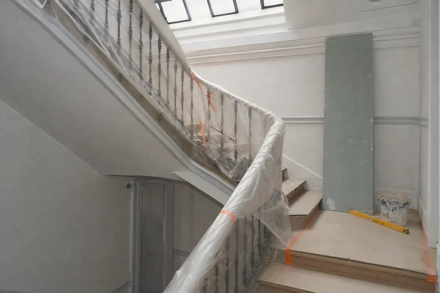 Cage d’escalier d’immeuble ancien protégée par des bâches pendant un chantier, main courante emballée